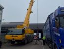 Yellow Mobile Crane Hoisting Operation Near Blue Truck on Industrial Site