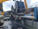 Gro&szlig;er Industriekran, der schwere Maschinen auf ein Transportfahrzeug auf einer Stra&szlig;e bewegt