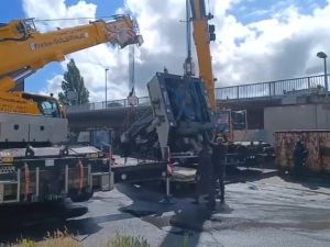 Large Machinery Being Lifted by Cranes Near an Urban Overpass