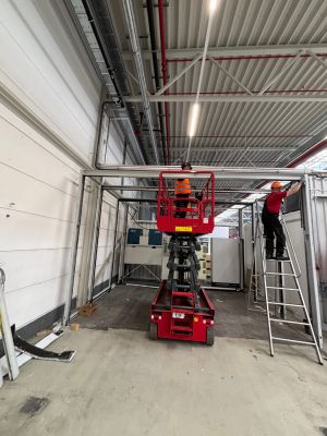 Bauarbeiter, die eine Scherenhebeb&uuml;hne und eine Leiter in einer industriellen Umgebung benutzen