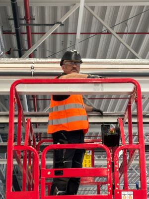 Bauarbeiter in Schutzausr&uuml;stung auf einer erh&ouml;hten Plattform in einer Lagerhalle