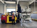 Arbeiter, der einen Gabelstapler in einem Industrielager bedient und gro&szlig;e Maschinen hebt